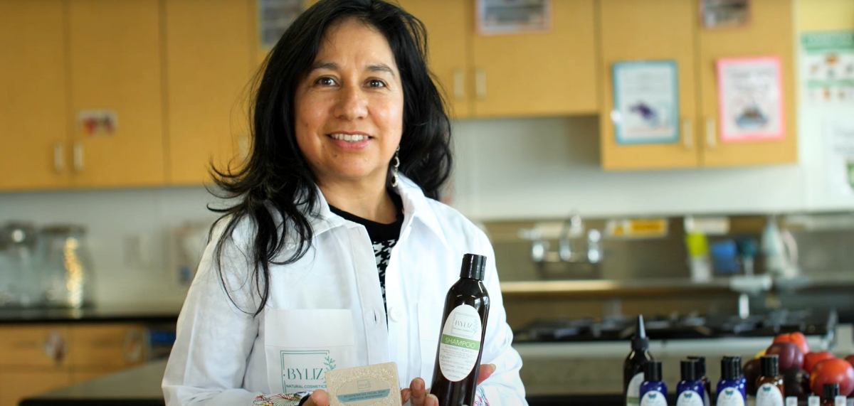 Elizabeth Elizabeth, wearing a white lab coat with her business's logo, holds up a soap and lotion.