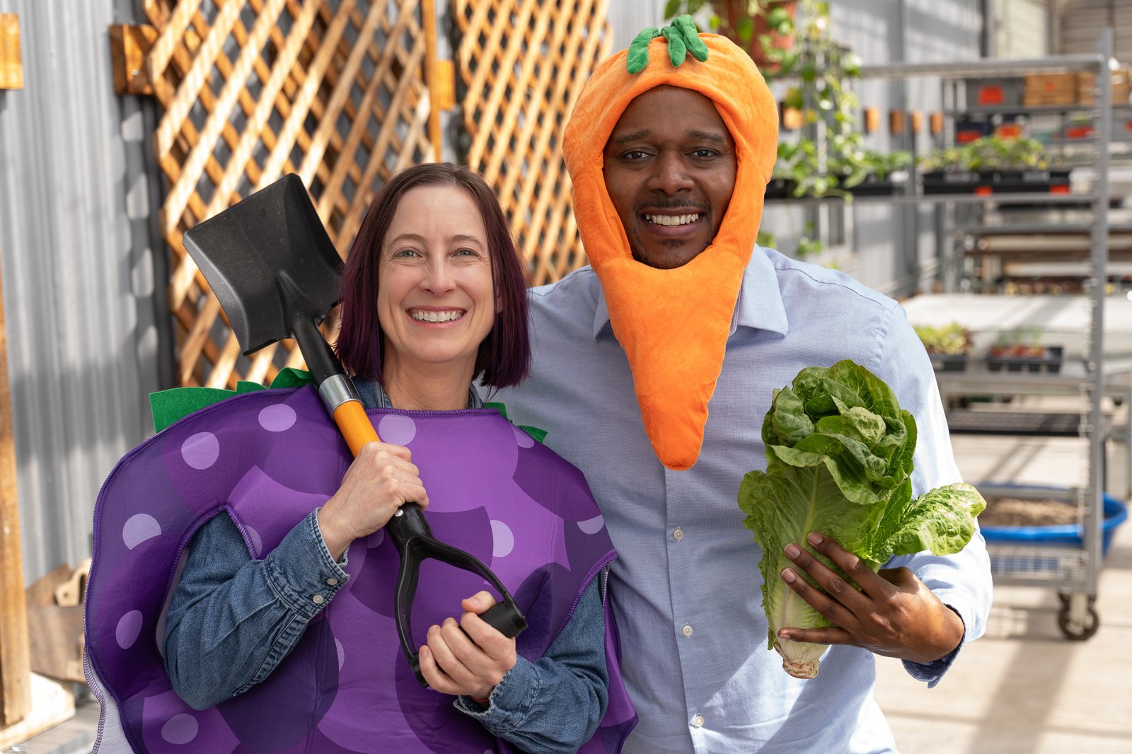 Erik & Teva 2 Teva, wearing a grape costume, holds a shovel over her shoulder, while Erik stands next to her with a carrot costume around his head while holding a head of lettuce.