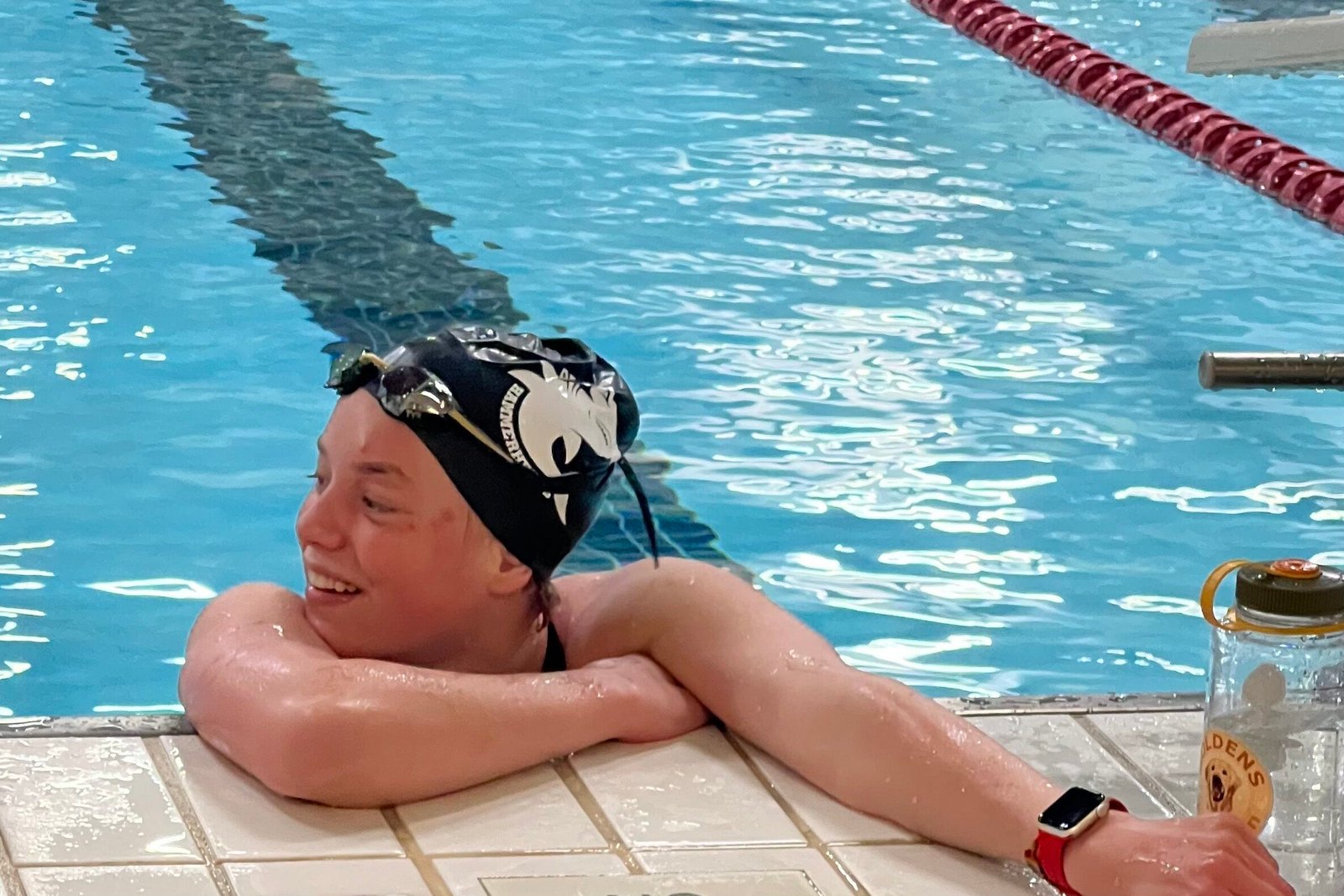 Sophia hangs on to the edge of the pool smiling and looking to the side.