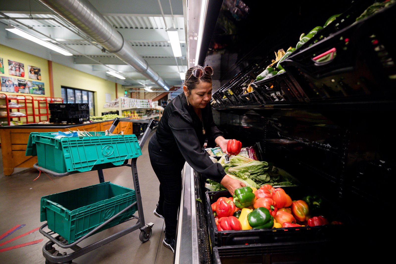 Woman picks up bell peppers from the Fresh Foods Market produce wall. 
