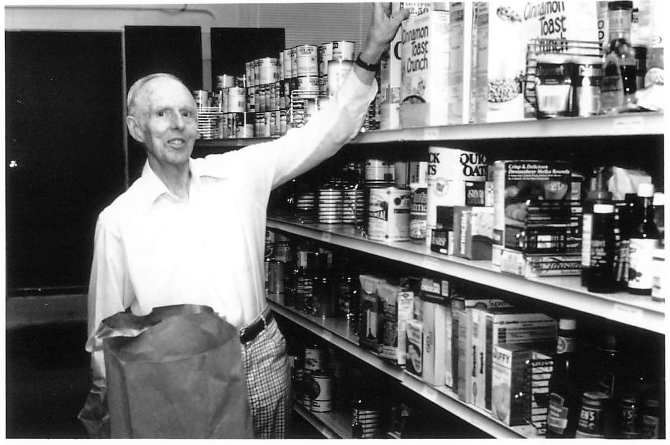 Black and white photo of a volunteer reaching for a box on full shelves at Metro Caring.