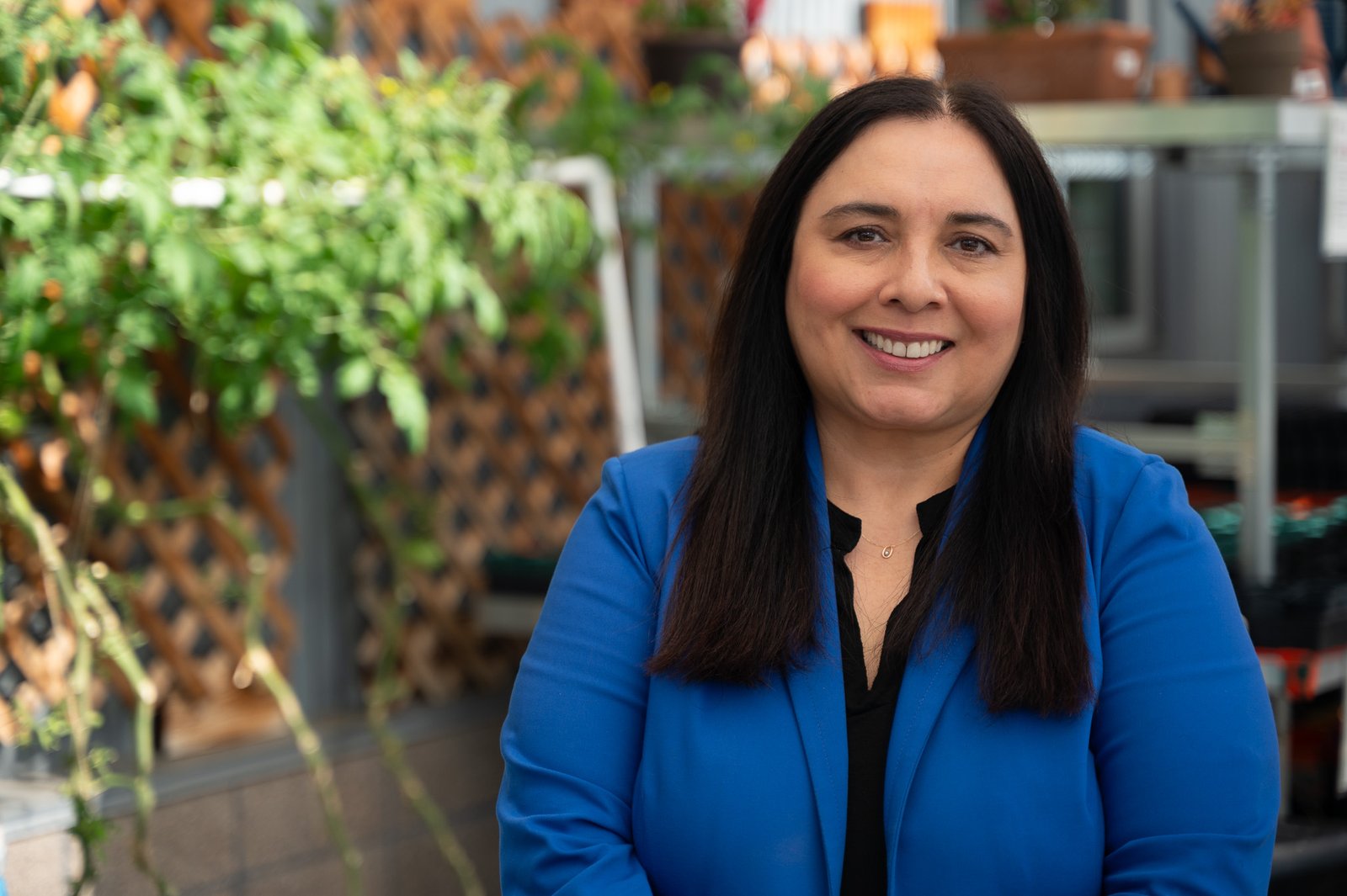 Lori_Casillas_landscape Lori poses for a headshot in the Metro Caring greenhouse. Tomato plants are out of focus behind her, contrasting nicely with her royal blue blazer.