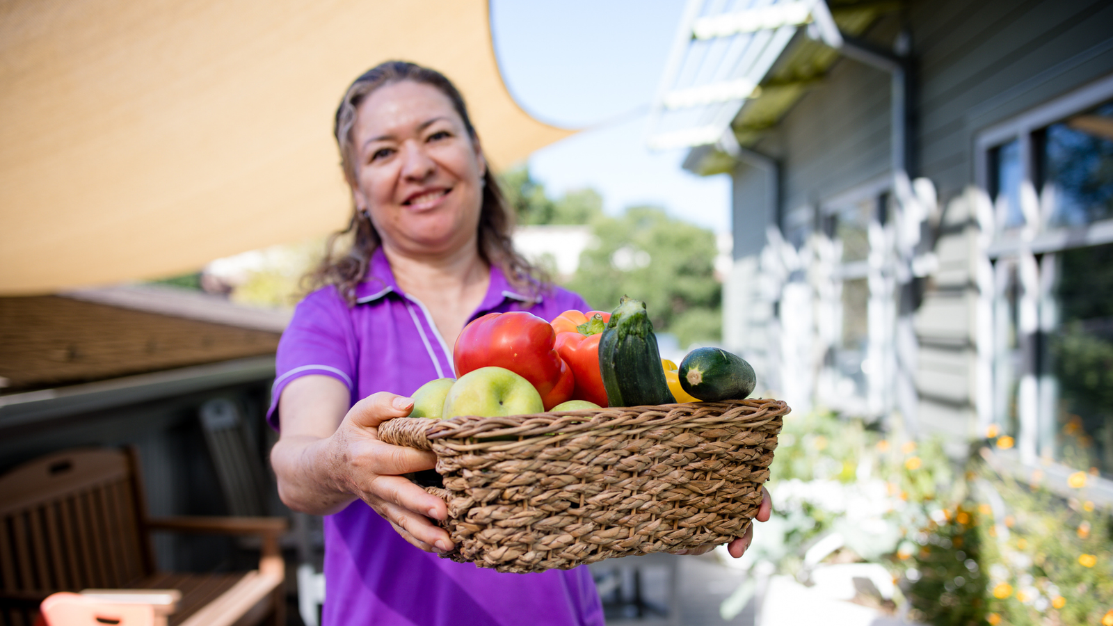 Woman holding out a basket full of vegetables like peppers and zucchinis.